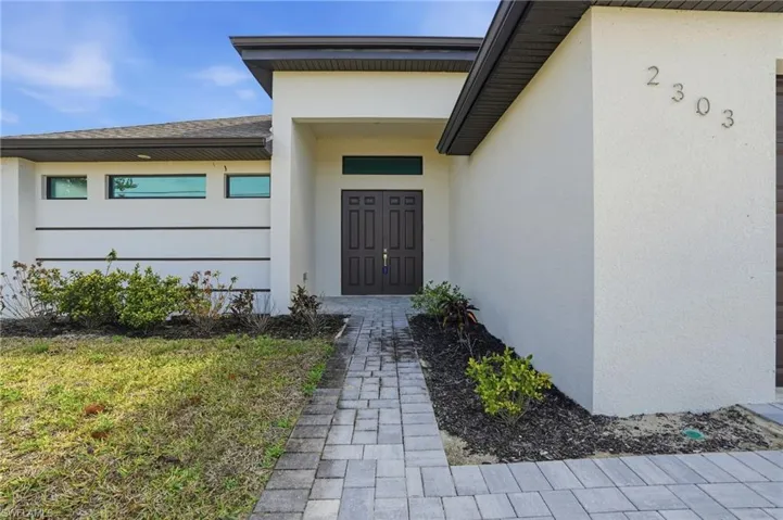 Property entrance featuring stucco siding, a shingled roof, and a yard