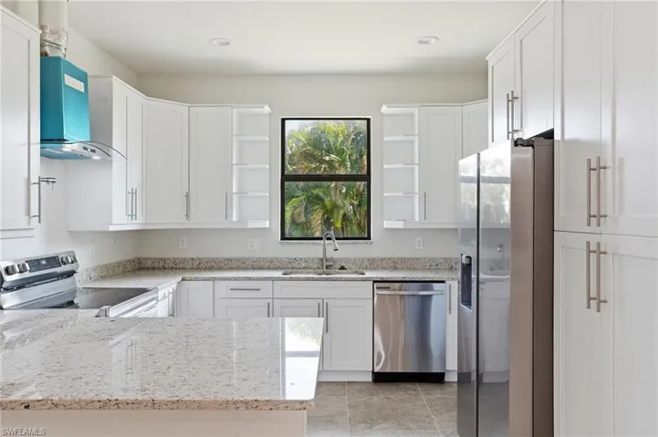 Kitchen featuring stainless steel appliances, white cabinets, light stone countertops, and open shelves