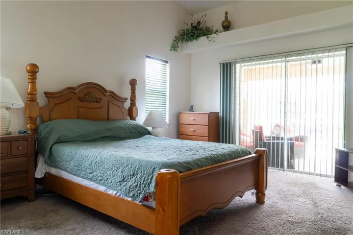 Carpeted bedroom featuring multiple windows, lofted ceiling, and access to exterior