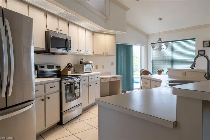 Kitchen featuring vaulted ceiling, stainless steel appliances, hanging light fixtures, sink, and light tile floors