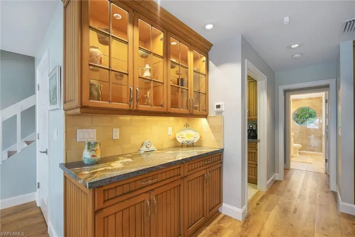 Bar with dark stone countertops, tasteful backsplash, and light hardwood / wood-style floors
