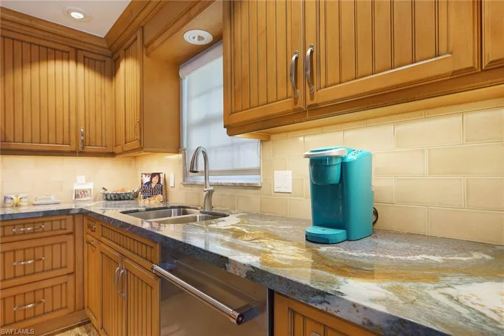 Kitchen with stainless steel dishwasher, stone countertops, backsplash, and sink