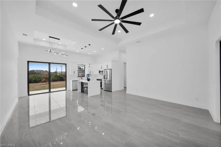 Unfurnished living room featuring a ceiling fan, a chandelier, and a raised ceiling