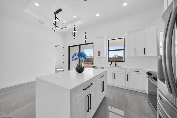 Kitchen with stainless steel appliances, white cabinets, a center island, hanging light fixtures, and a tray ceiling