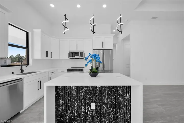 Kitchen with stainless steel appliances, light stone counters, white cabinets, and a center island