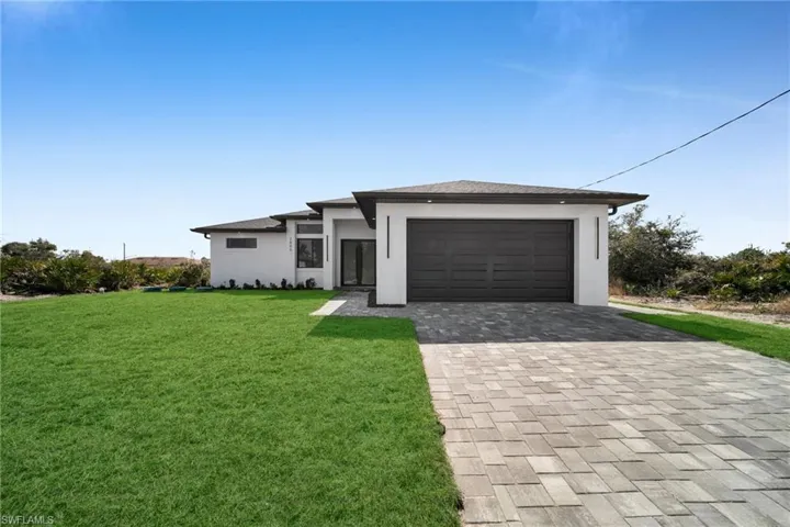 Prairie-style house with decorative driveway, stucco siding, a front lawn, and an attached garage
