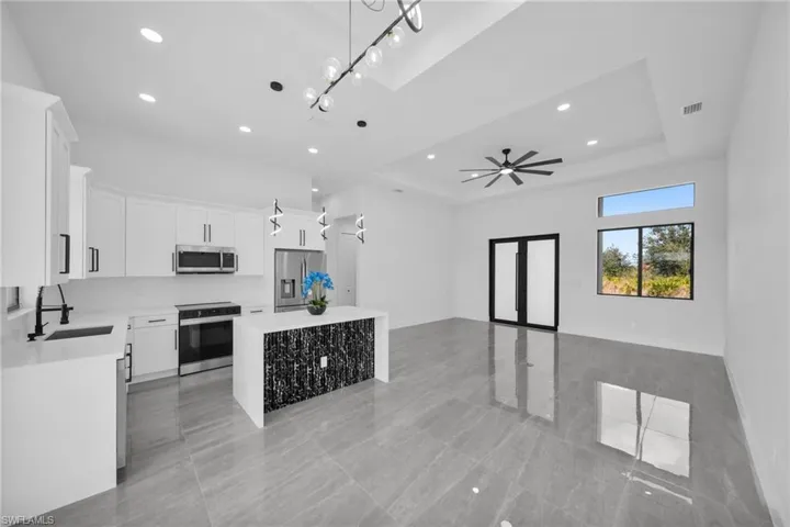 Kitchen with white cabinetry, stainless steel appliances, pendant lighting, light stone countertops, and open floor plan