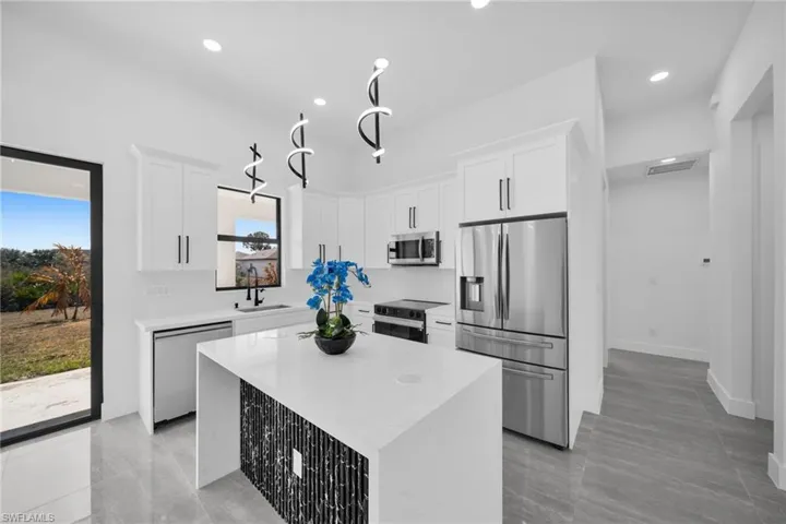 Kitchen with stainless steel appliances, white cabinets, a kitchen island, light stone countertops, and recessed lighting