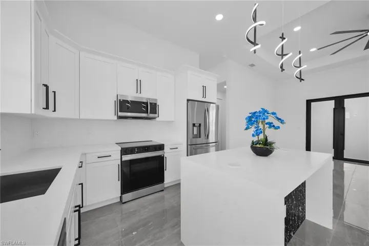 Kitchen with a kitchen island, light stone countertops, stainless steel appliances, and white cabinetry