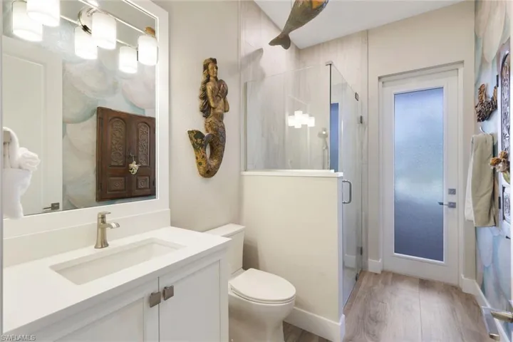 Bathroom with toilet, a shower with door, vanity, and hardwood / wood-style flooring
