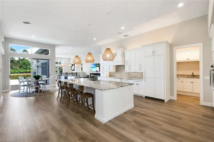 Kitchen with pendant lighting, dark wood-type flooring, light stone countertops, an island with sink, and white cabinetry
