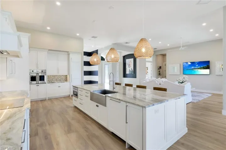 Kitchen with white cabinetry, sink, stainless steel appliances, hanging light fixtures, and a spacious island