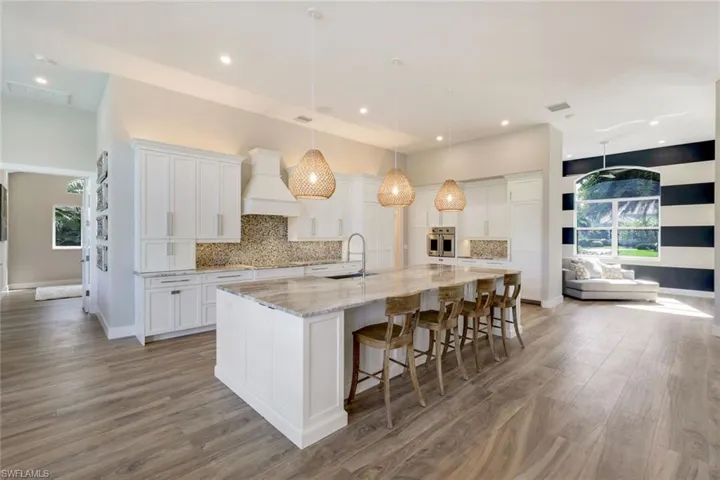 Kitchen featuring white cabinets, custom exhaust hood, plenty of natural light, and a large island with sink