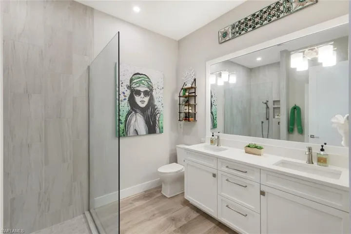 Bathroom featuring tiled shower, wood-type flooring, vanity, and toilet