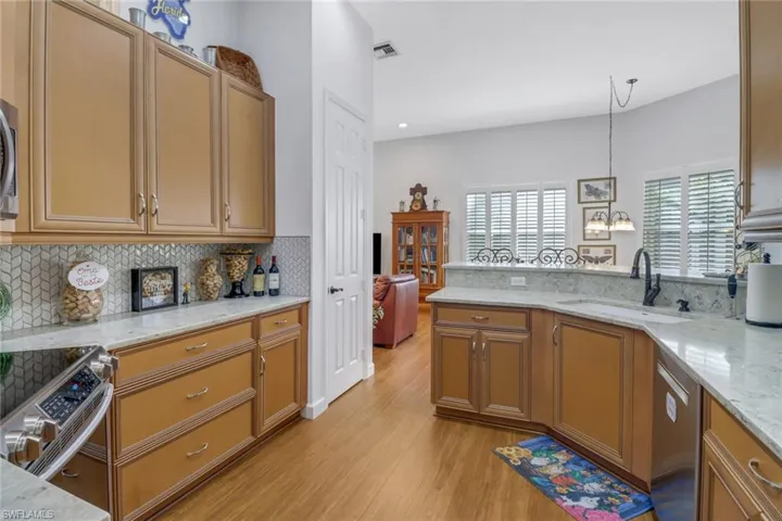Kitchen featuring pendant lighting, appliances with stainless steel finishes, sink, light hardwood / wood-style floors, and light stone counters