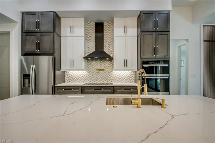 Kitchen with light stone countertops, stainless steel appliances, wall chimney exhaust hood, white cabinetry, and backsplash