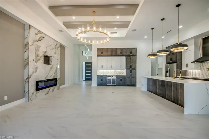 Unfurnished living room featuring a raised ceiling, sink, beverage cooler, an inviting chandelier, and a fireplace