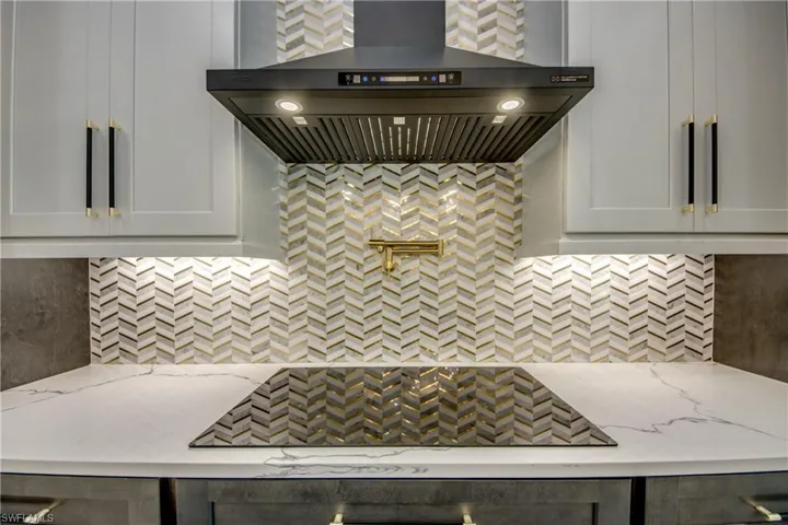 Kitchen featuring tasteful backsplash, wall chimney range hood, light stone counters, and white cabinetry