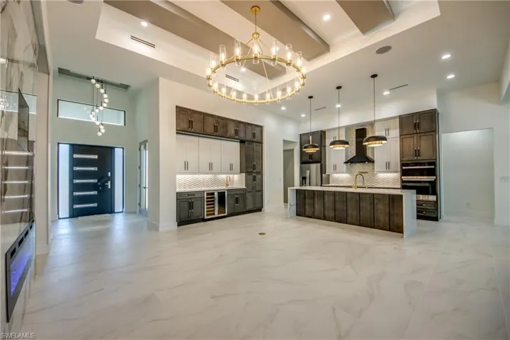 Kitchen featuring decorative backsplash, a raised ceiling, stainless steel fridge, pendant lighting, and wall chimney range hood