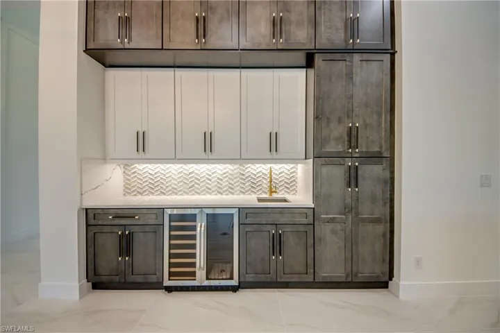 Bar featuring decorative backsplash, beverage cooler, sink, and dark brown cabinetry