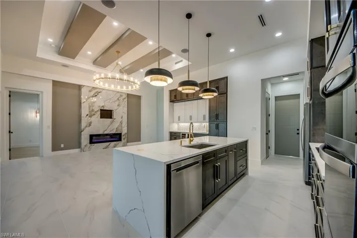 Kitchen featuring sink, light stone countertops, hanging light fixtures, appliances with stainless steel finishes, and an island with sink