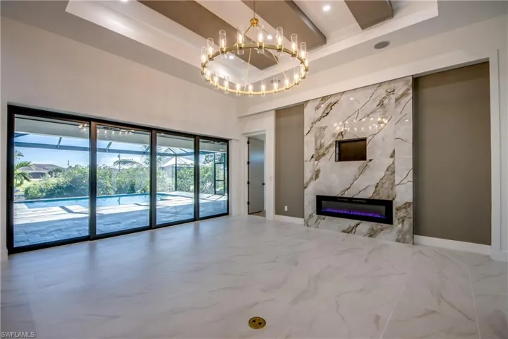Unfurnished living room featuring a fireplace, a wealth of natural light, a tray ceiling, and a chandelier