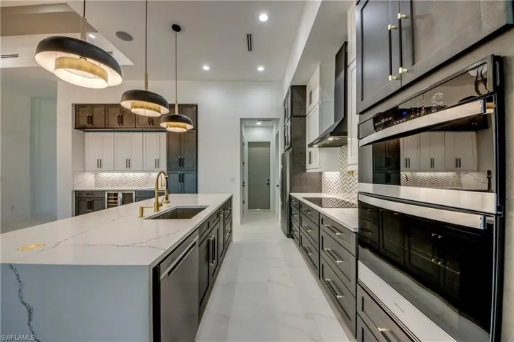Kitchen featuring sink, wall chimney range hood, a large island, appliances with stainless steel finishes, and decorative light fixtures