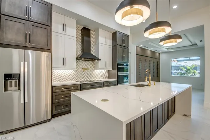 Kitchen with wall chimney exhaust hood, a center island with sink, black appliances, and sink