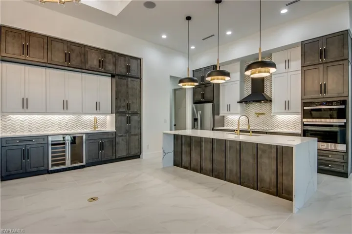 Kitchen featuring pendant lighting, tasteful backsplash, wine cooler, an island with sink, and appliances with stainless steel finishes