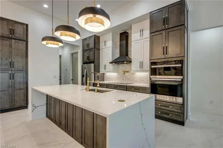 Kitchen with sink, a kitchen island with sink, backsplash, wall chimney range hood, and appliances with stainless steel finishes