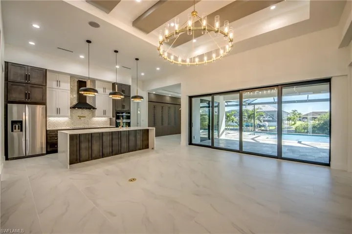 Kitchen featuring backsplash, stainless steel refrigerator with ice dispenser, hanging light fixtures, and wall chimney range hood