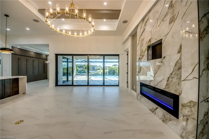 Unfurnished living room featuring an inviting chandelier, a tray ceiling, a high ceiling, and a high end fireplace
