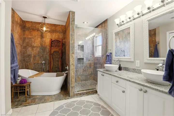 Full bath with double vanity, a soaking tub, a stall shower, and light tile patterned floors