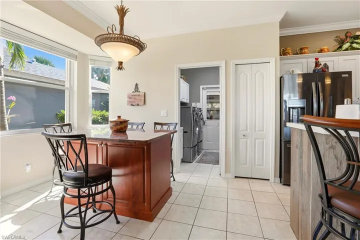 Kitchen with a breakfast bar area, stainless steel fridge, hanging light fixtures, crown molding, and light tile patterned floors