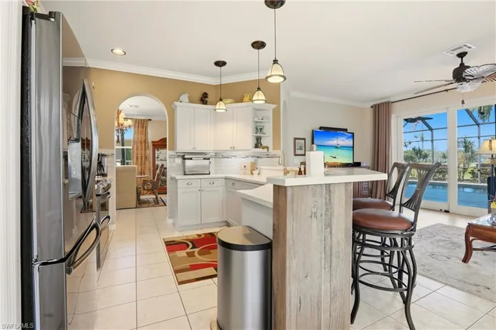 Kitchen with stainless steel appliances, light countertops, light tile patterned flooring, decorative light fixtures, and crown molding