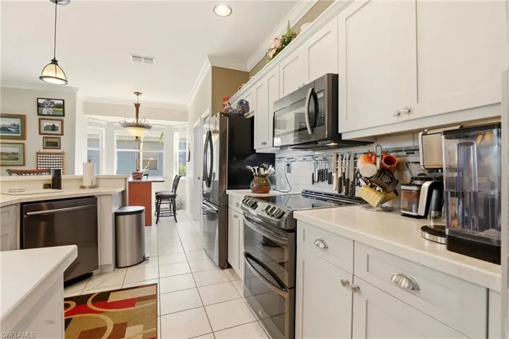 Kitchen with stainless steel appliances, decorative light fixtures, crown molding, white cabinets, and decorative backsplash