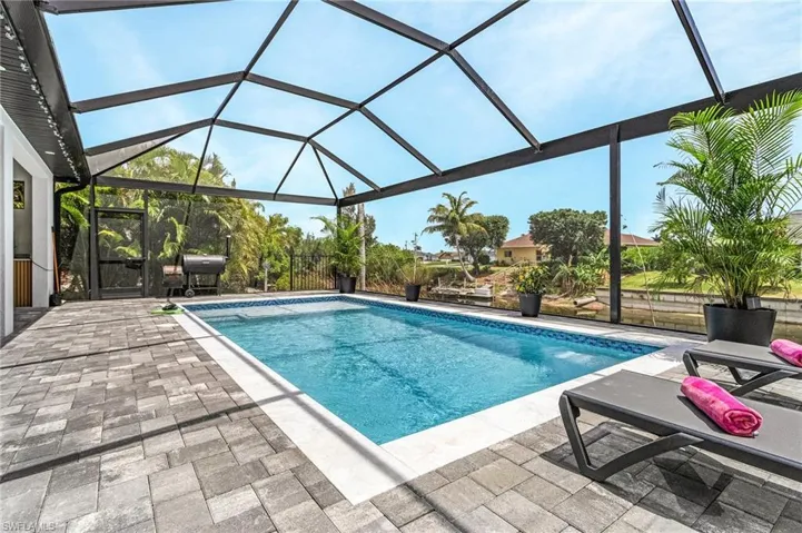 Outdoor pool with glass enclosure, a patio area, and grilling area