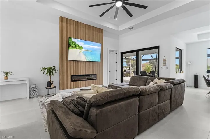 Living area with a ceiling fan, visible vents, a large fireplace, concrete flooring, and a raised ceiling