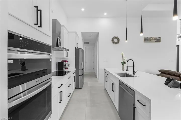 Kitchen featuring appliances with stainless steel finishes, a sink, light countertops, white cabinets, and wall chimney exhaust hood