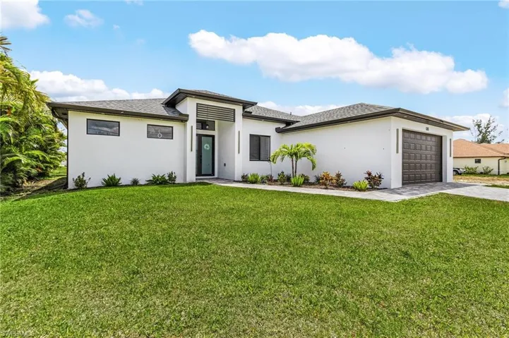 Prairie-style home with an attached garage, driveway, stucco siding, and a front yard