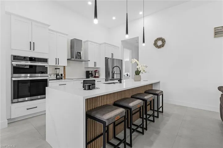 Kitchen featuring a breakfast bar area, appliances with stainless steel finishes, white cabinetry, a sink, and wall chimney exhaust hood