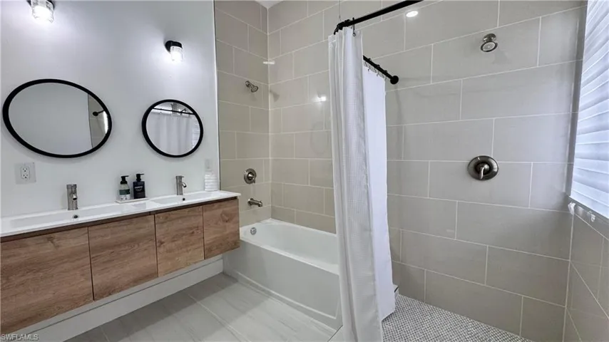 Bathroom featuring double vanity, tile patterned floors, and tiled shower / bath
