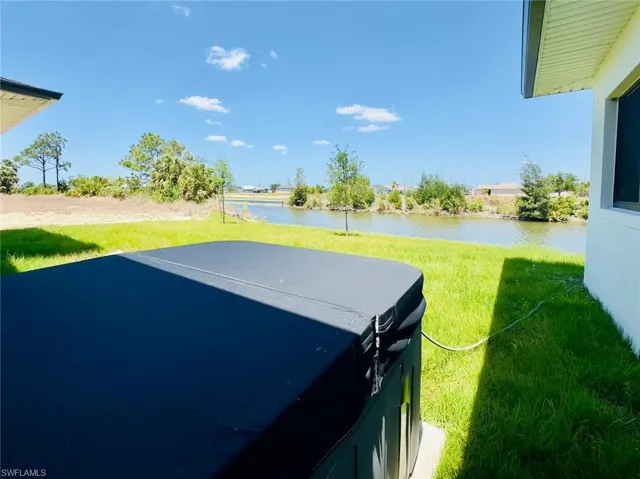 View of green lawn with a water view, a hot tub, and a patio