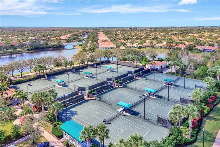 Multiple tennis courts with green hard surfaces, surrounded by mature landscaping and a perimeter fence