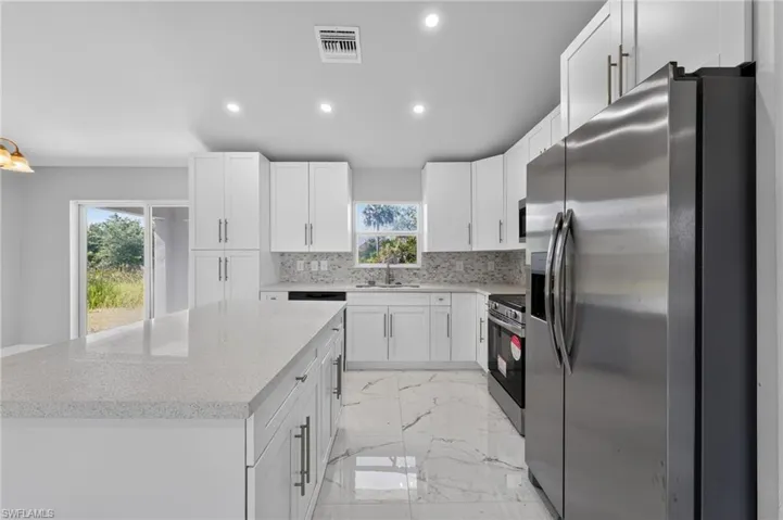 Modern kitchen featuring white shaker cabinetry, stainless steel appliances, a spacious island with a light-toned countertop, and white tile flooring