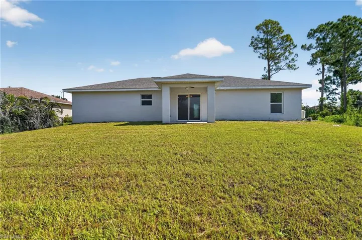 Expansive rear yard featuring green lawn, concrete block construction, and sliding glass doors
