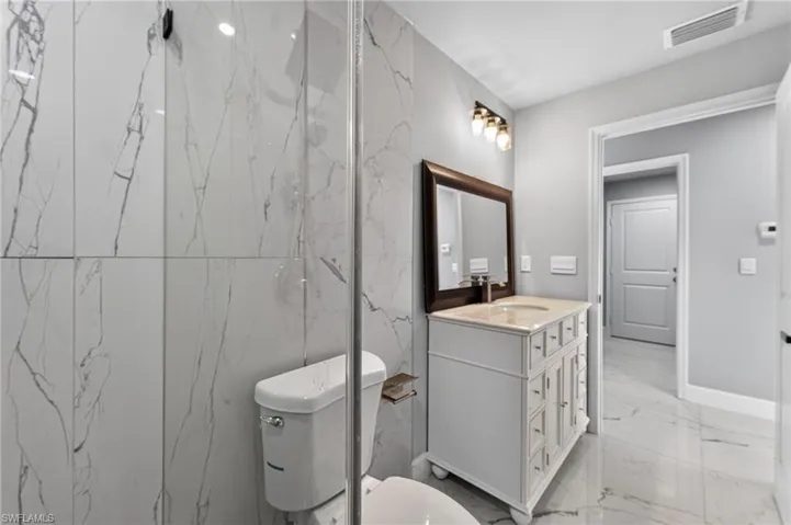 Bathroom featuring large format marble-look tile walls and flooring, a white vanity with a light-colored countertop and integrated sink, a framed mirror, and a three-bulb vanity light fixture