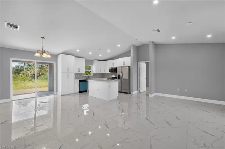 Open-concept living space featuring high ceilings, large format tile flooring, a modern kitchen with white cabinetry and stainless steel appliances, and sliding glass doors leading to the outdoors