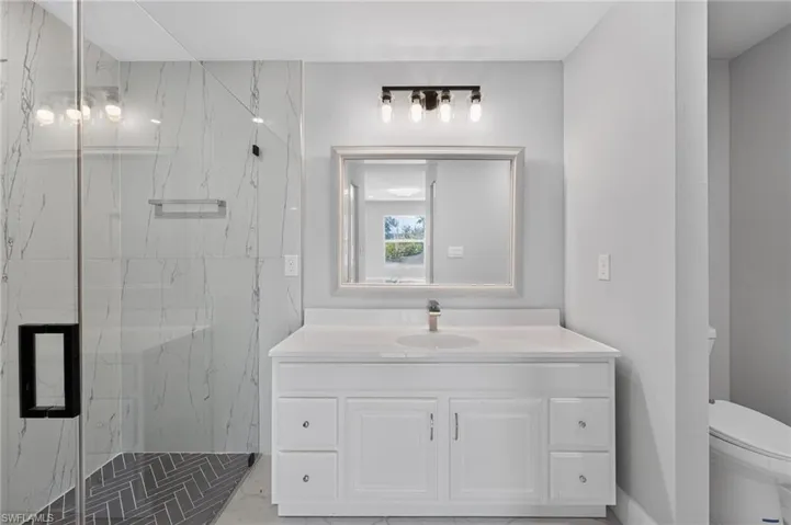 White vanity with a single basin sink, light countertop, and framed mirror