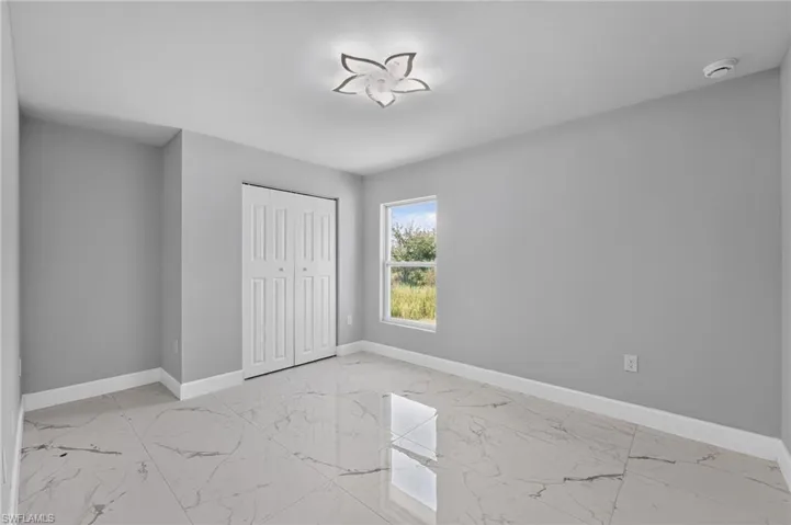 Bright room featuring large format tile flooring, a window with outdoor scenery, closet with bi-fold doors, white baseboards, and a decorative ceiling light fixture